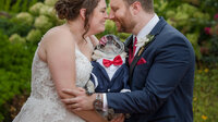 Couple snuggling and holding a pug, sharing a near kiss over the dog’s head during their wedding.