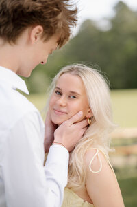 Leaning against a wall, a man holds his fiancé's waist as she looks into his eyes. They're standing under a pointed arch.