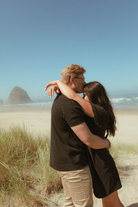 An engaged couple pose together for a portrait on Cannon Beach. The man kisses his fiancé on the forehead.