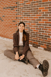 woman sitting on the ground smiling with a brick wall in the background