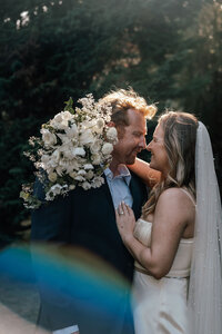 Bride and groom Olivia & Daveduring their wedding portraits in a lush garden, with golden sunset light streaming through and a rainbow just below them, photographed by Auckland wedding photographer Zanthe Vorsatz.