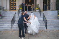 Most Valuable Bridesmaid Day-of Coordinators behind the scenes at New Jersey wedding helping NJ bride walk up the stairs to the ceremony holding the train of her dress. 