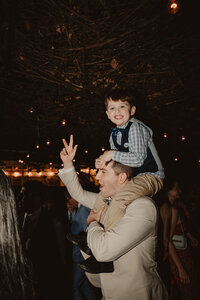 A person holding a small child on their shoulders while they both smile 