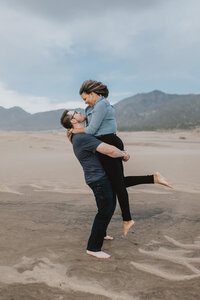 man holds woman on sand dunes