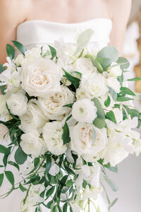 A bride holds her bouquet that is overflowing with white and green florals.
