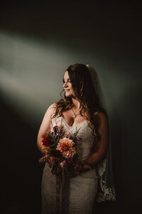 A person in a wedding dress holding a bouquet of flowers with a light stream coming down on them 