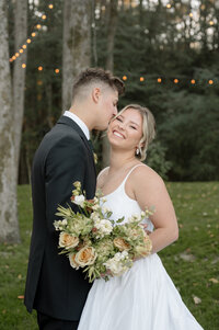 A black and white photo of a bride and groom at their wedding reception. They're wearing matching sneakers and sitting on the floor against a wall, kissing.