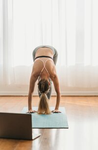 An impressive display of flexibility and strength, showcasing an individual in a forward-bending yoga posture with sunlight spilling into a serene, airy room.