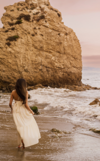 girl at the beach running away from camera wearing a long white dress and she has long dark hair