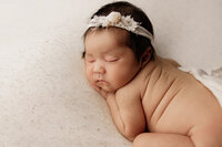 Newborn baby girl with a floral headband sleeping on a soft mauve blanket with her hands gently tucked under her cheek.
Photograph by Yucaipa newborn photographer Kaitlyn Dawn Photography.