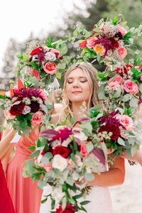 Bride standing with her eyes closed as bridesmaids hold up their bouquets around her head, framing her