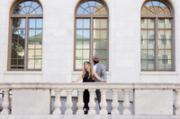 Fiances pose for engagement photos in front of a large elegant building