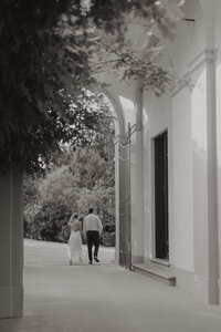 An intimate and luxurious wedding moment in Italy, where the bride and groom share a quiet walk through a historic venue, exuding sophistication and love.