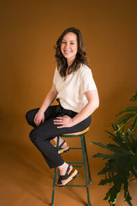 Melonie, founder of Grassroots Creative Company, smiling while sitting on a stool, ready to partner with clients on their web design journey.