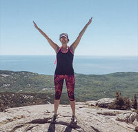 Alison Seponara arms up in the air on top of a mountain