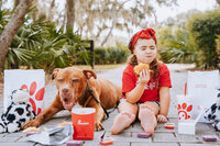 baby girl sitting next to dog on the ground with chick fil a