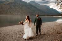 Traveling Wedding Photographer, couple walking along a lake with mountains in the background