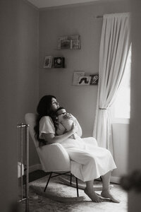 New mom cradling her newborn while sitting in the nursery with soft window light.