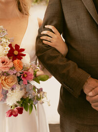 detail shot of brides arm wrapped around her grooms arm focused on her ring and bouquet
