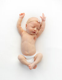 newborn baby stretches on white bean bag
