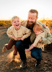 Dad kneeling down playing with sons in Phoenix desert at sunrise