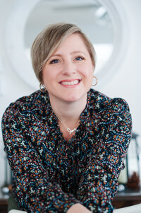 Headshot of Kristin Palkoner owner of Lens and Prism Personal Branding Photography, smiling, wearing a dark colorful shirt and love necklace.
