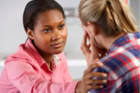 Woman talking to another woman, hand placed on shoulder as if to be comforting her.