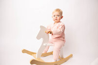 two year old girl on a wooden rocking horse against a white backdrop.
