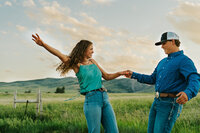 A man holding his girlfriend's hand. She is leaning slightly backwards and they are having fun, laughing a little bit.