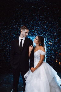 A bride looks up at her groom while holding his arm as they stand silhouetted by off camera flash