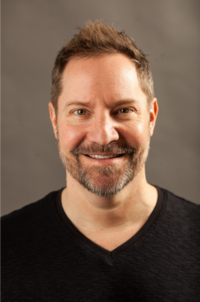 Jessica wearing a white blazer, smiling as she writes in her planner
