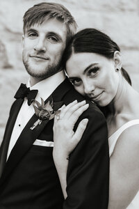 A person standing behind their partner resting their head on their shoulder as they both smile.