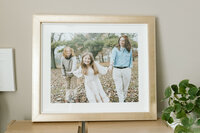 Three framed portraits stand together up against a wall with various textures and colors such as wood, metal, light wood