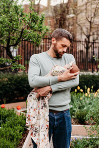 New dad cradling his swaddled newborn baby in his arms.  The baby's swaddle is draped and hanging down in front of dad.  Photo taken during Philadelphia Newborn Photography session
