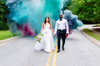 An interracial couple during their luxury elopement in Irmo, SC, walking through a stunning cloud of teal and purple smoke. A bold, vibrant moment at the wedding of Murphy Holloman.