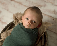 Newborn boy looking up wide awake in a wooden bucket.