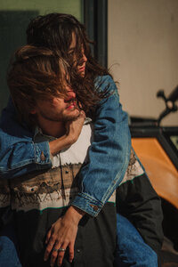 Badass cowboy couple pose on a tractor together with the wind moving their hair.