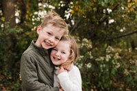 Two smiling children embracing outdoors in a family photography package session.