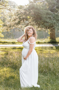 stunning mom to be standing near a iron gate wearing a white long dress huging her 35 week pregnant belly phot by elizabeth klusmann photography