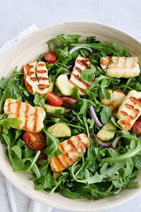 one bowl of salad with arugula, grilled halloumi,  and tomatoes