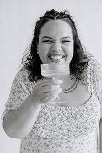 A person smiling and holding a cocktail glass to their lips