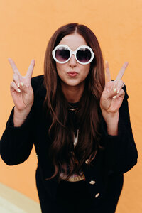 Andrea Wilde, CEO and founder of the LIVE BIG Collective, posing confidently with sunglasses on and peace signs