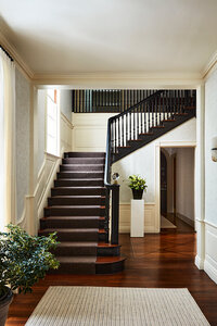 Interior decorators in Boston created a modern look in a historic Concord estate foyer with a black grand stair, cream walls, and geometric wallpaper blending old and new.