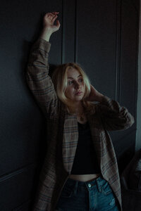 A woman is leaning up against a black wall with her arm up and looking past the camera.