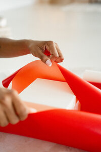 Hands wrapping a box with bright red wrapping paper