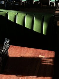 A green leather restaurant booth with dramatic light and shadow