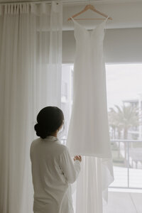 bride looks at hanging wedding dress
