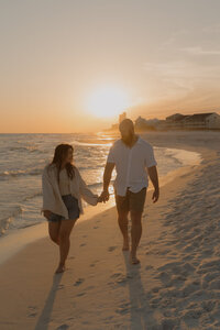 Michaela and her husband walking on the beach in Santa Rosa Beach, FL at sunset with the golden sun in the background. 