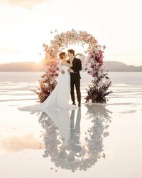 Utah Wedding Photographers capture bride and groom standing in front of floral arch