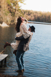 a groom picking up a bride as they elope in upstate new york in a lake with mountains in the background